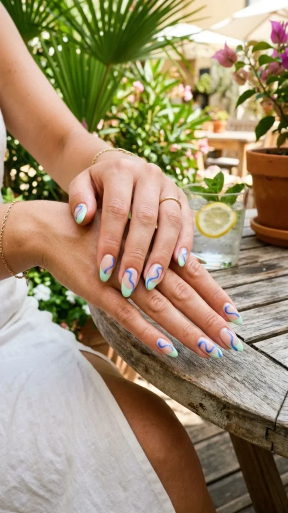 Pastel green French nails with artistic blue squiggle accents.