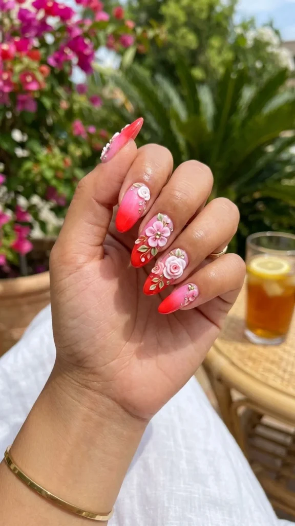 Red to pink ombre nails finished with elegant 3D floral accents.
